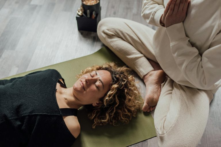 Relaxed woman meditating on yoga mat with another person praying beside her indoors.