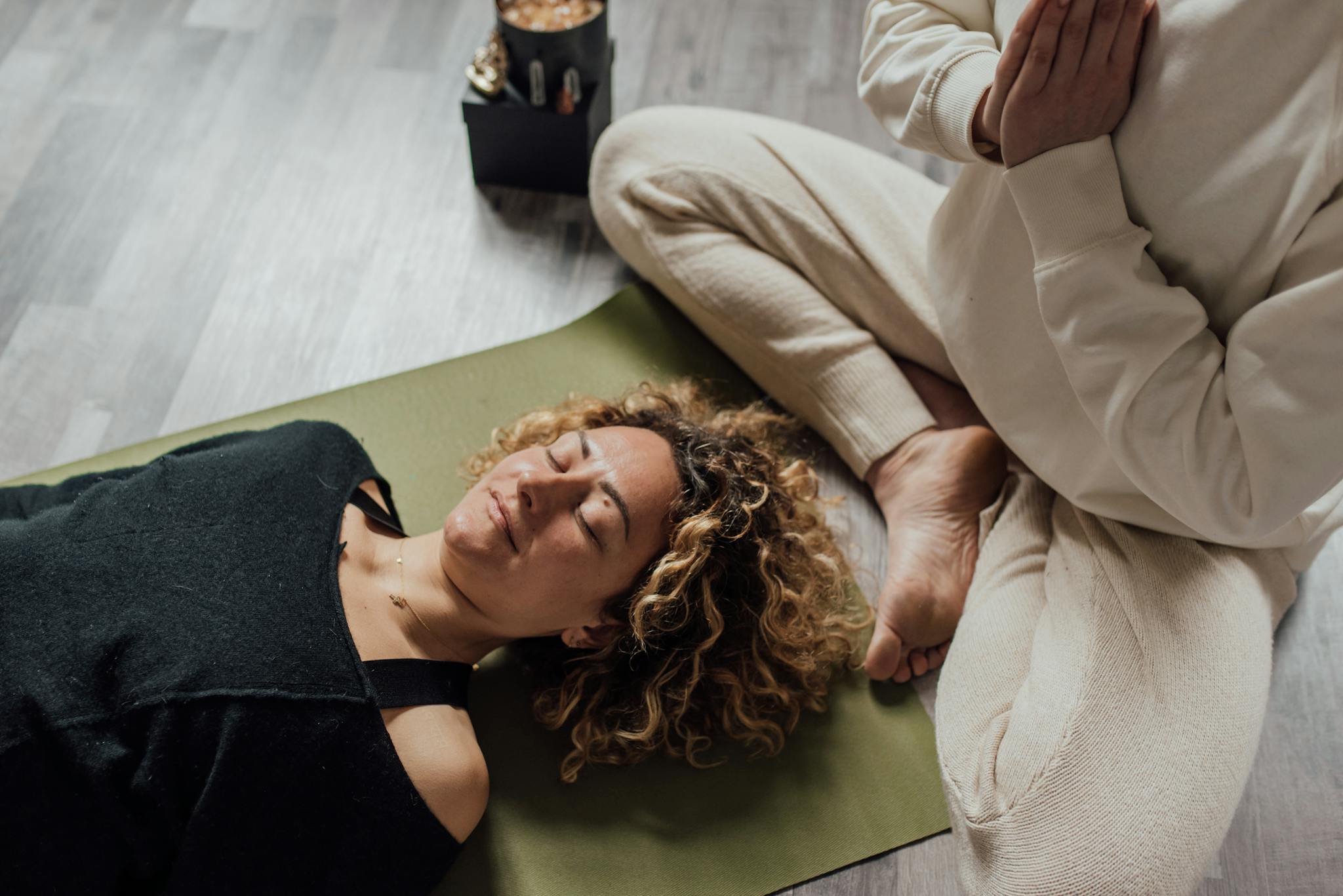 Relaxed woman meditating on yoga mat with another person praying beside her indoors.