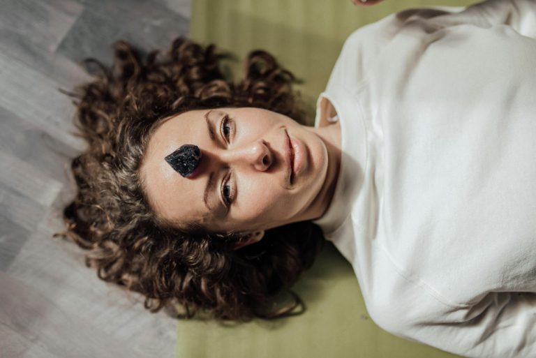 Young woman lying down with a healing crystal on her forehead, promoting relaxation and meditation.